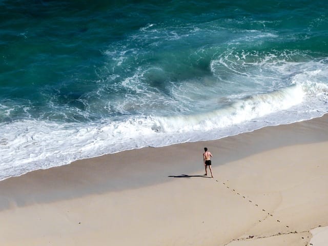 homme qui marche sur le sable vers la mer en laissant des traces de pas